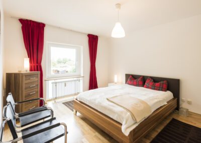 Immobilienfotograf München – Stilvolles Schlafzimmer mit roten Vorhängen und Holzrahmenbett