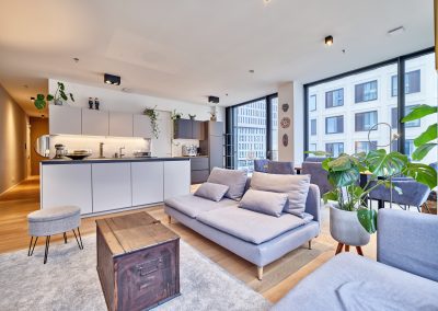 Immobilienfotograf München – Wohnbereich mit Sofa, moderner Küche und großen Fenstern